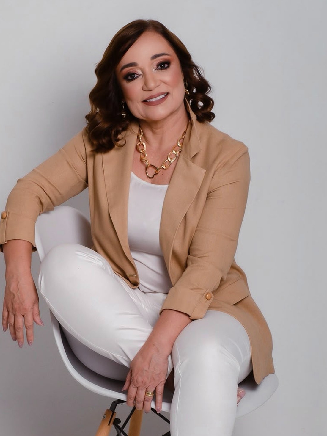 Andrea Tenório sentada, em roupas claras, olhando para a câmera